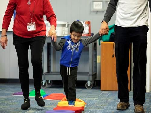 Two adults assisting child in TR Tots program