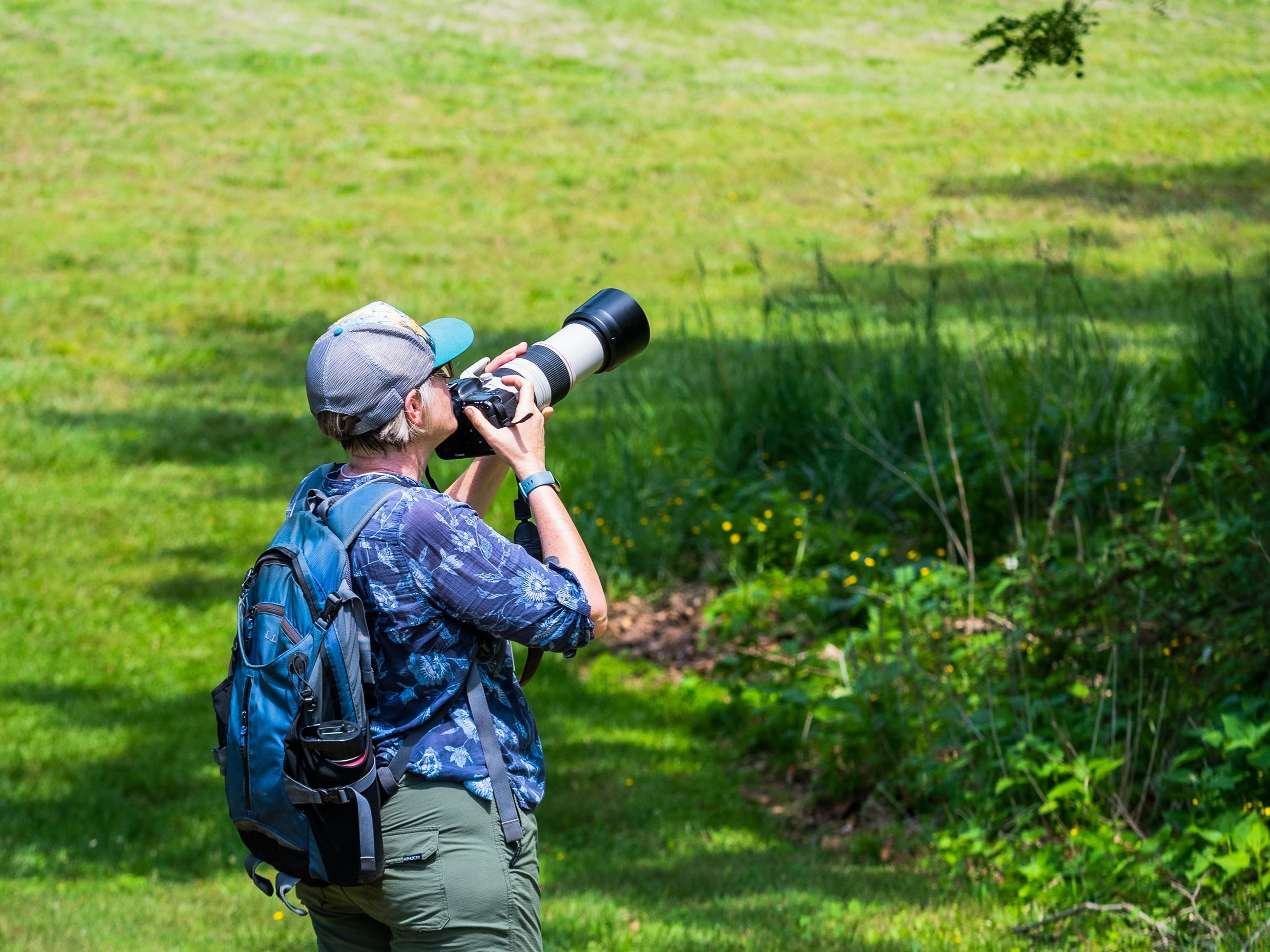 Woman in a field looking through a camera with a long lense