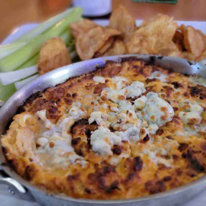 Buffalo chicken dip topped with blue cheese and sides of chips and celery