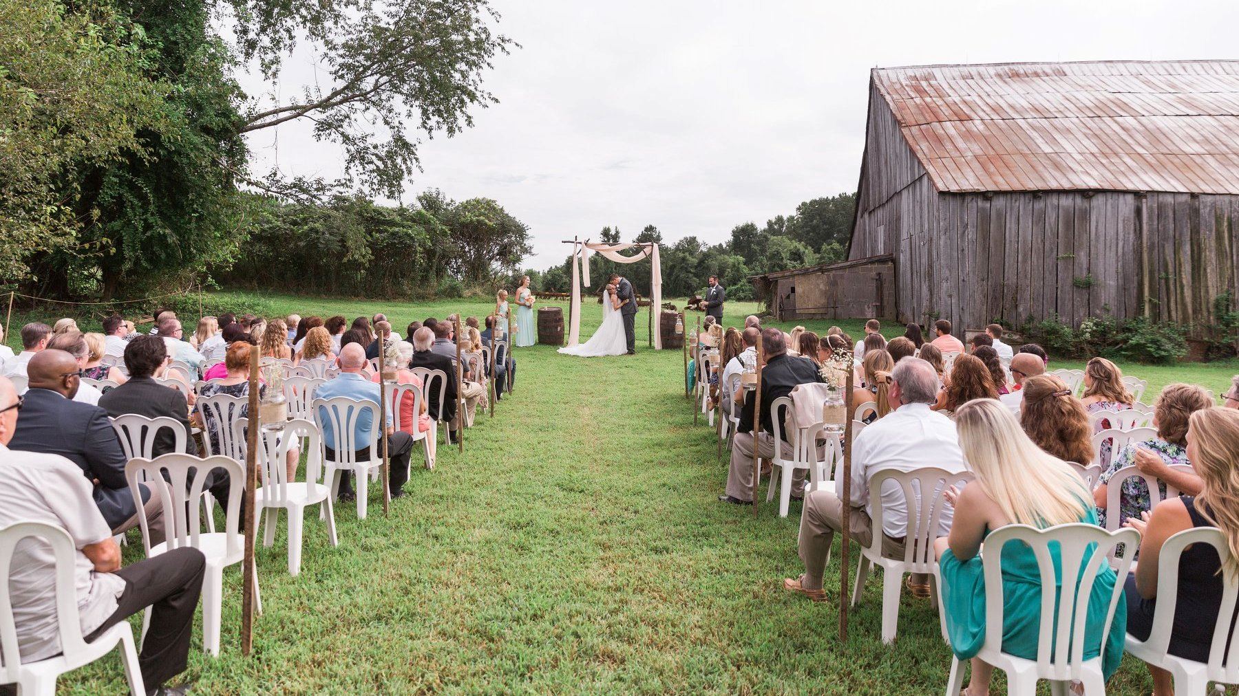 Bride and groom getting married in front of a barn and flower arch